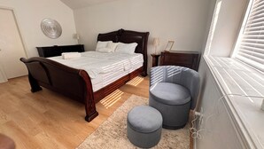 A bedroom with a wooden bed, a grey upholstered chair, and a small ottoman. - Your Arlington Hotspot: Games, Flights & Family Fun (Arlington)