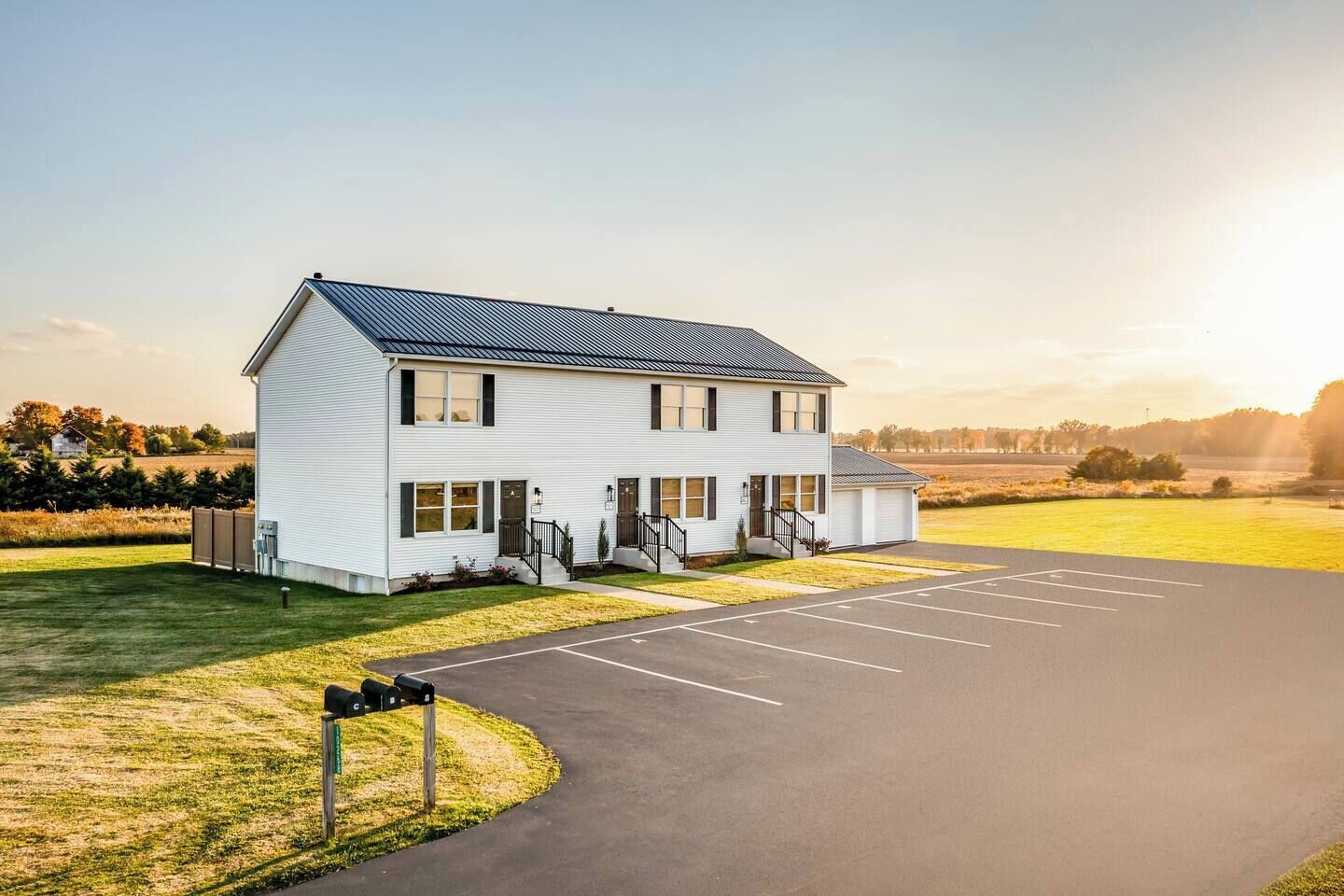 A two-story building with a covered parking area and a grassy field in the background.