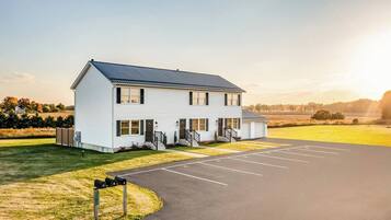 A two-story building with a covered parking area and a grassy field in the background.