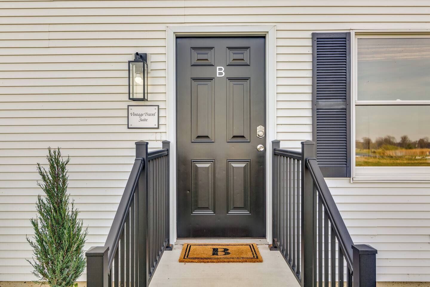 A front door with a 'B' marking, a small sign reading 'Vintage Travel Suite', a mailbox, a window with shutters, and a doormat.