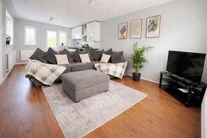 A modern living room with a grey sofa set, a grey ottoman, a flat-screen TV, and a potted plant. - The Serene Retreat in Manchester (Manchester)