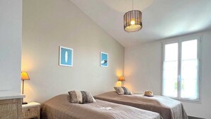 Ein Schlafzimmer mit zwei Betten, einem Schminktisch und einem Fenster mit Tageslicht.