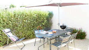 Eine Außenpatio mit Tisch, Stühlen, einem Grill und einem Sonnenschirm.