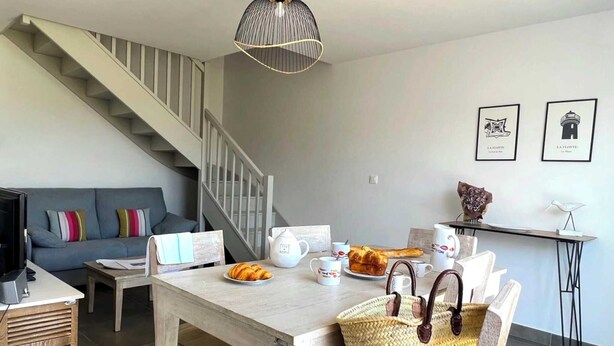 Ein modernes Wohnzimmer mit Treppe, einem Essbereich mit Frühstückstisch und einer Couch mit bunten Kissen.