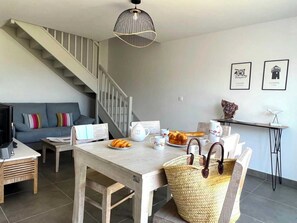 A modern living room with a staircase, a dining area with a table set for breakfast, and a sofa with colorful cushions. - Villa No. 3 - Le Petit Bec   (La Flotte)