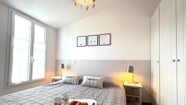 Une chambre à coucher avec un lit, des tables de chevet, une fenêtre et des œuvres d’art murales.