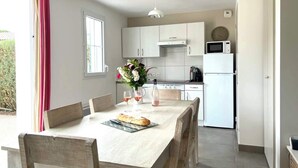 Une cuisine moderne avec des meubles blancs, un four à micro-ondes et une cuisinière. On y trouve une table à manger avec des chaises et un vase de fleurs.
