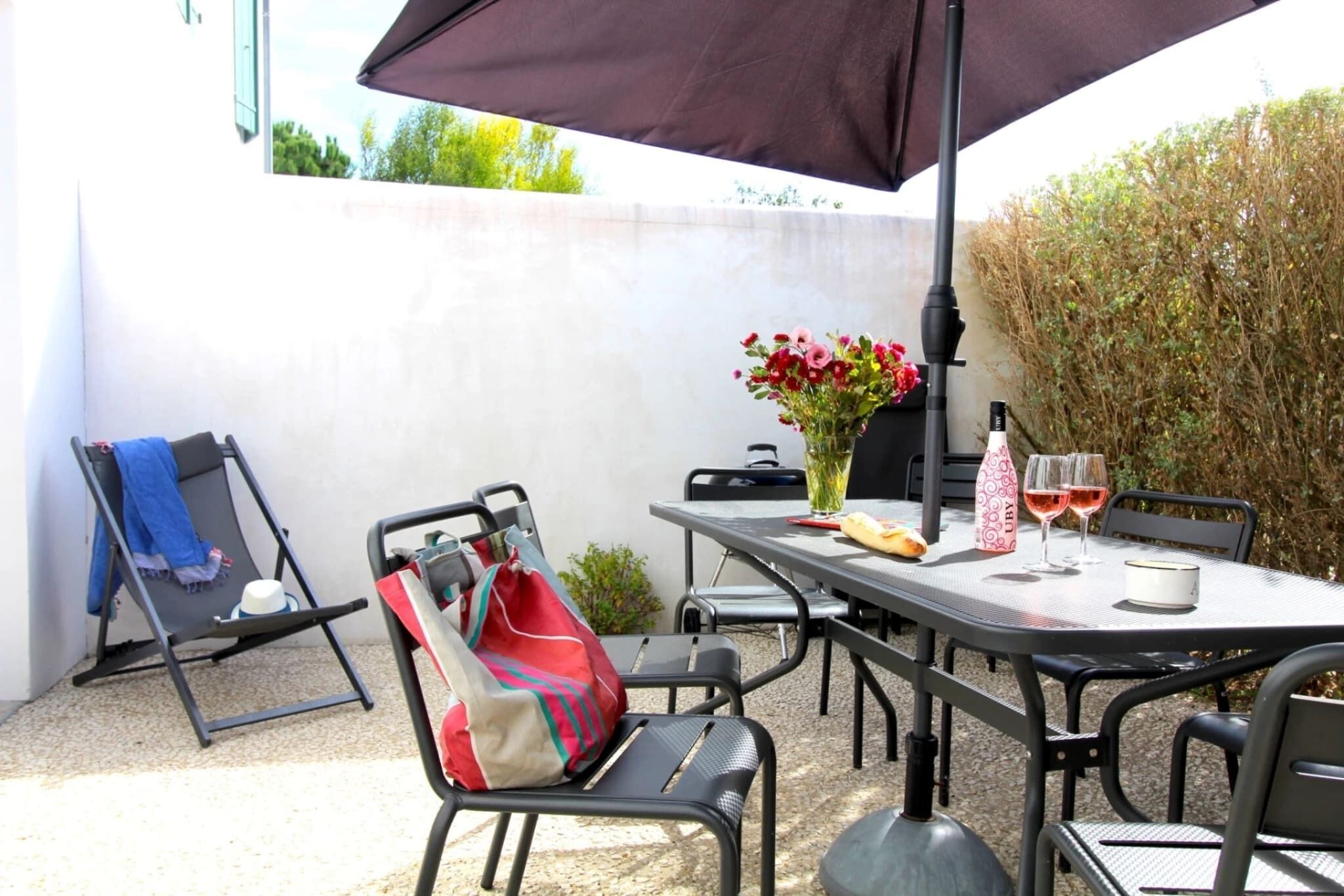 An outdoor patio with a table set for two, a chair, a red bag, and a vase with flowers.