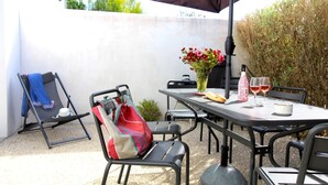 Une terrasse extérieure avec une table dressée pour deux personnes, une chaise, un sac rouge et un vase rempli de fleurs.