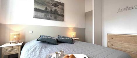 Une chambre avec un lit, des tables de chevet, un plateau avec des croissants et un tableau au mur.