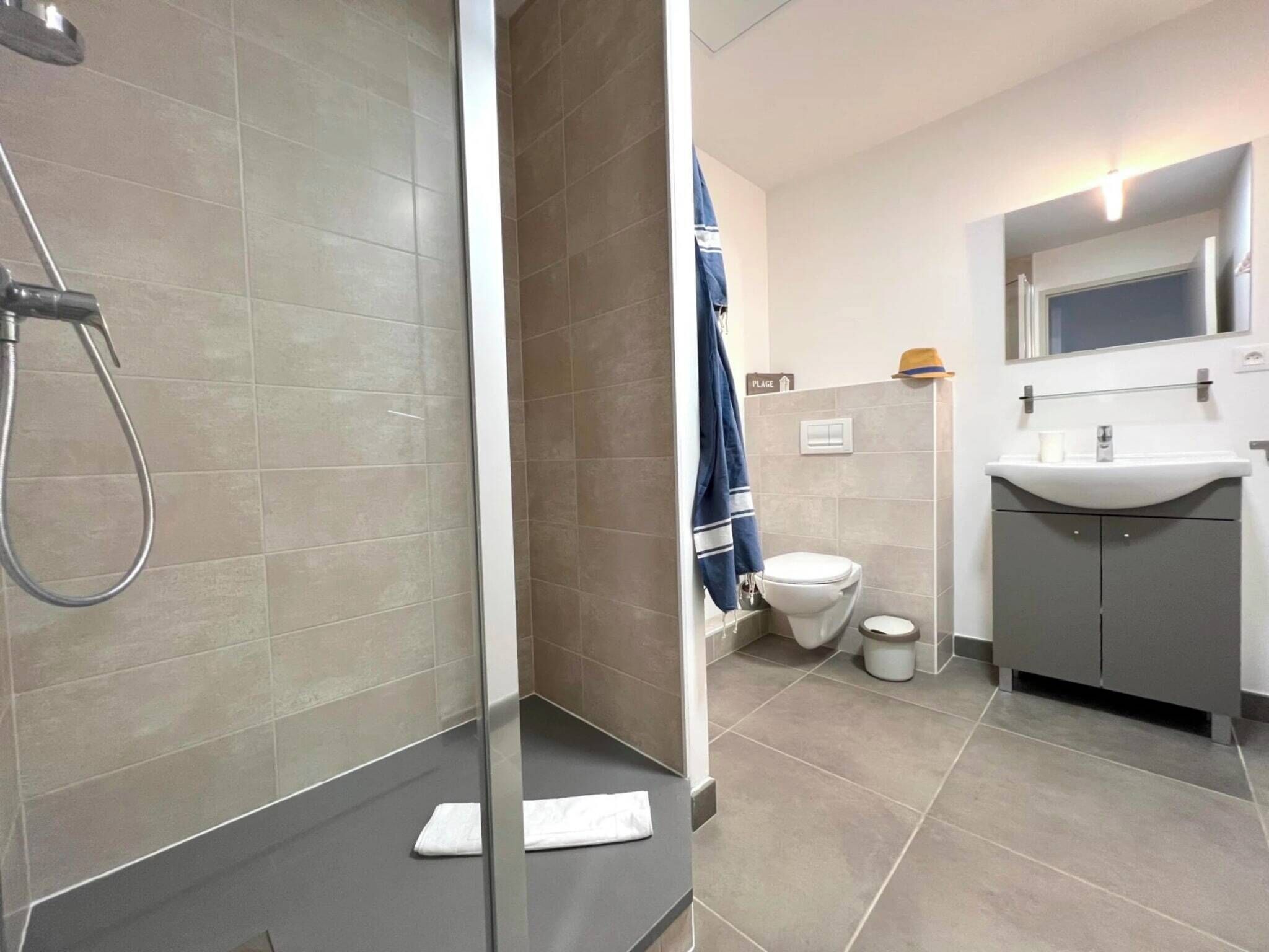 Et moderne badeværelse med brusekabine i glas, toilet og vask med spejl over.