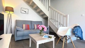 A living room with a grey sofa, a coffee table with a magazine, a white chair, and a staircase. - Villa n°8 - The little sergeant (La Flotte)