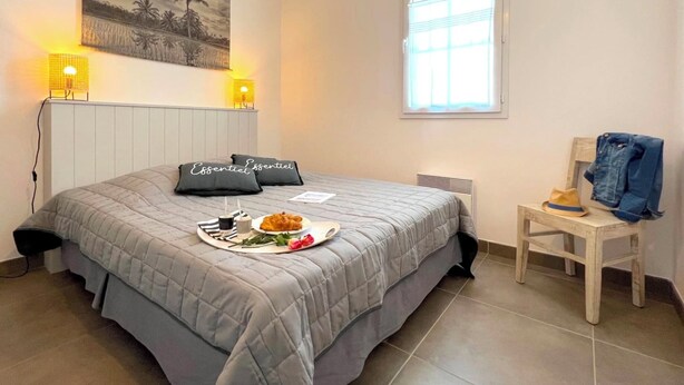 A bedroom with a bed, two bedside lamps, a window, a radiator, a chair, and a wall with a painting. - Villa n°8 - The little sergeant (La Flotte)