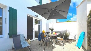 A patio area with a table, chairs, a large umbrella, and a blue surfboard leaning against the wall. - Villa n°8 - The little sergeant (La Flotte)