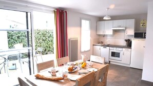 A dining area with a table set for two, a kitchen with white cabinets, a microwave, and an oven. - Villa n°8 - The little sergeant (La Flotte)