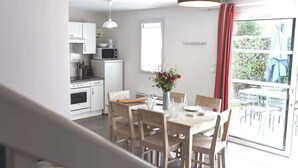Una cocina moderna con electrodomésticos blancos, un comedor con sillas y mesa de madera, y vistas al exterior a través de un ventanal corredero.