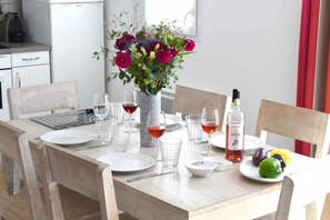 Et spisebord dækket med tallerkener, glas, bestik og en vinflaske, samt en blomstervase og et fad med frugt.