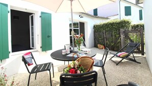 An outdoor patio with a round table, chairs, a wicker basket with flowers, and a large umbrella. - Villa n°6 - The Target (La Flotte)