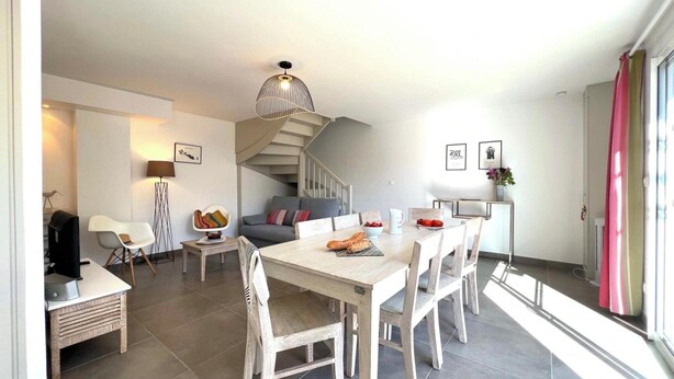 A modern kitchen with a dining area, a staircase, and a view of the outside. - Villa n°5 - Les gollandières (La Flotte)