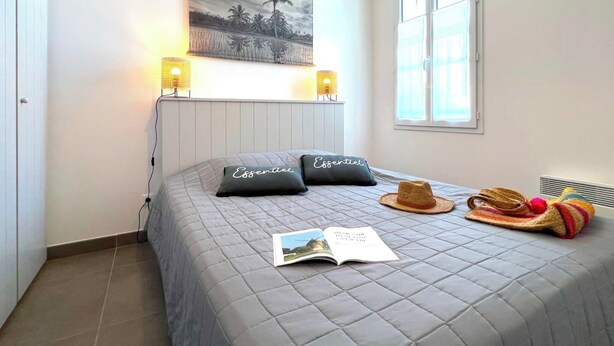 A bedroom with a bed, a painting, two bedside lamps, a hat, and a book. - Villa n°9 - Le martray (La Flotte)