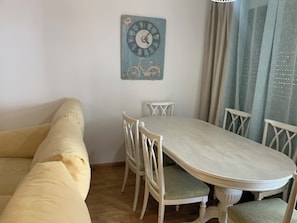 A dining area with a white table and chairs, a blue wall clock, and a sofa.