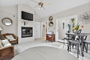 A living room with a fireplace, a television, wicker furniture, and a dining area with stools. - Mystic  Retreat | Hot Tub & Lake Harmony Access (Lake Harmony)