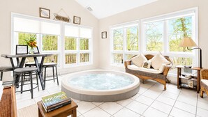 Ein Zimmer mit Whirlpool, einem Esstisch mit Stühlen, einer Couch und großen Fenstern mit Blick auf Grünflächen.