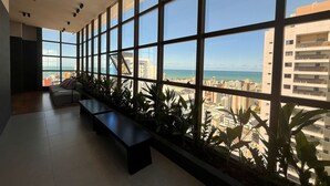 A modern interior with large windows, a bench, and potted plants. - Flat Quality Comfort CoHouse - Tambaú (João Pessoa)