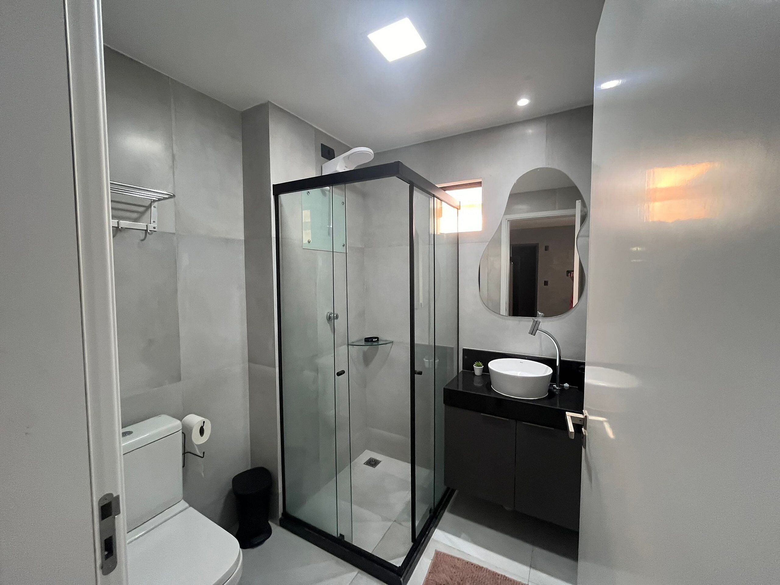 A modern bathroom with a glass-enclosed shower, a white toilet, a black sink, and a mirror with an oval frame.