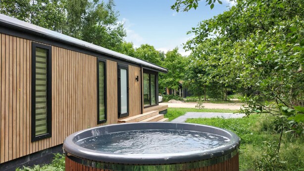 Un edificio moderno de madera con amplios ventanales y un jacuzzi al frente.