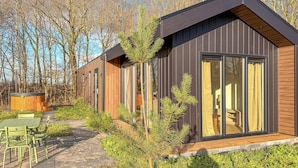 Une cabane moderne dotée de grandes fenêtres, d’un revêtement extérieur en bois et d’un espace patio avec des sièges d’extérieur.