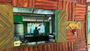 A rustic kitchen with wooden walls, a green countertop, and a person cooking. - Ceiba Ganadito (Drake Bay)