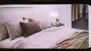 Un letto rifatto con cura, coperto da una coperta a righe e con numerosi cuscini, un comodino con una lampada e una piccola pianta, e una testiera a muro.