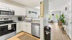 Una cocina moderna con armarios blancos, microondas, estufa y lavavajillas. Se ve un cartel con la palabra "HELLO" en la pared.