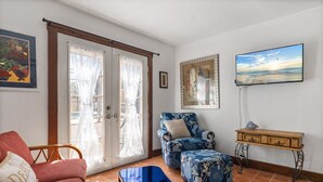 Un salon avec un canapé, un fauteuil, une petite table et un téléviseur fixé au mur.