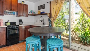 Une cuisine compacte avec des meubles en bois, une cuisinière et un évier. On y trouve une table ronde avec des chaises bleues et une fenêtre avec des rideaux.