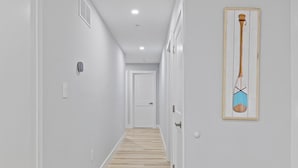 Un couloir étroit avec un plancher en bois, des murs blancs et une porte au fond.