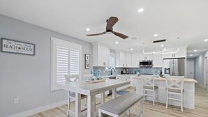 Une cuisine moderne avec des meubles blancs, un îlot central et un ventilateur de plafond.