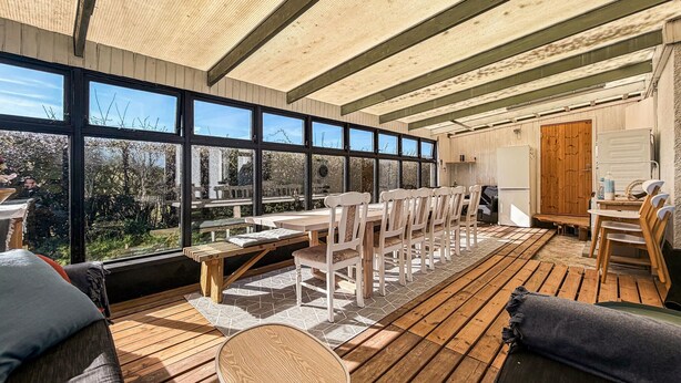 Une terrasse en bois avec un espace repas, de grandes fenêtres et un coin cuisine.