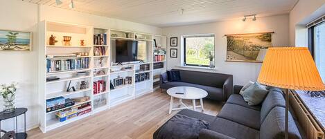 Ein Wohnzimmer mit einer Couch, einem Fernseher, Bücherregalen und einem Fenster.