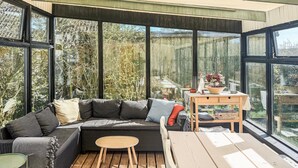 Une pièce moderne dotée d’un grand mur de verre, d’un canapé, d’une table ronde et d’une terrasse en bois.