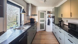 Une cuisine moderne avec un plancher en bois, des appareils électroménagers en acier inoxydable et une fenêtre donnant sur un jardin.