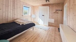 Une chambre à coucher avec un lit, une table de chevet, une fenêtre, une porte et un petit ventilateur.