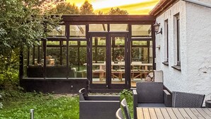 Une terrasse extérieure dotée d’une plateforme en bois, de meubles en osier et d’une véranda en verre offrant une vue sur le jardin.