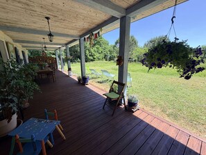 Eine überdachte Terrasse mit Holzboden, Gartenmöbeln und hängenden Pflanzen.