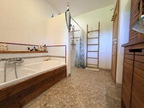Ein Badezimmer mit Badewanne, Dusche, Fliesenboden, Holzregalen und einem Holzschrank.