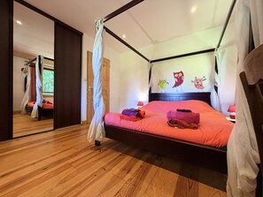 Ein Schlafzimmer mit Baldachinbett, Holzboden und einem Spiegel, der den Raum widerspiegelt.