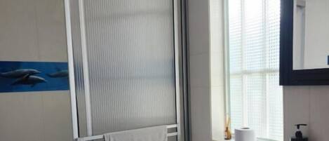 A bathroom with a shower, toilet, sink, and a window with blinds.