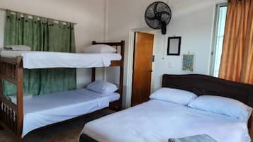 Una habitación con dos literas, una cama individual, un ventilador, una puerta y una ventana con cortinas.
