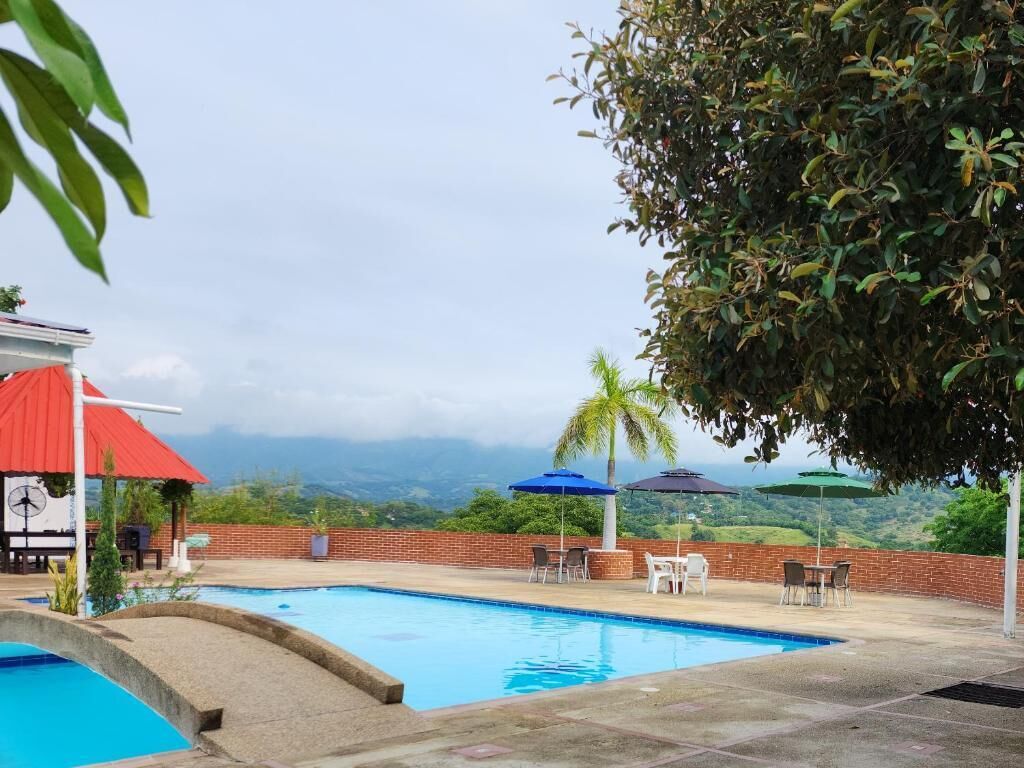 A swimming pool with a view of mountains, a red-roofed structure, and outdoor seating with umbrellas.